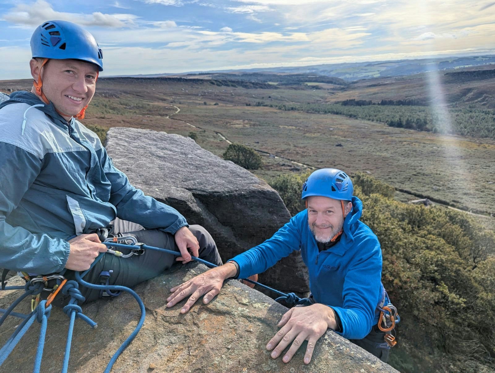 Lead climber belaying their second to the top of a Peak District gritstone crag