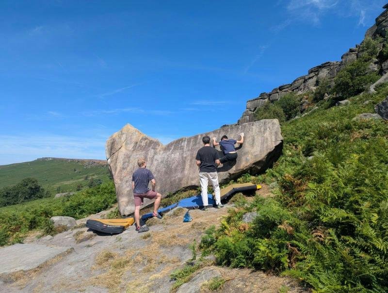 Boulderers with crash pads below a gritstone boulder in the Peak District