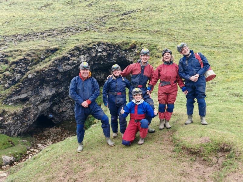 A family in caving oversuits and helmets outside a Peak District cave entrance