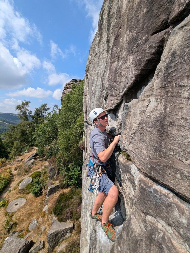Climber on a gritstone arete above the trees in the Peak District