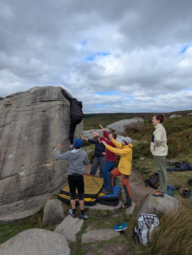 A small group bouldering on a gritstone boulder on a Peak District edge with an instructor